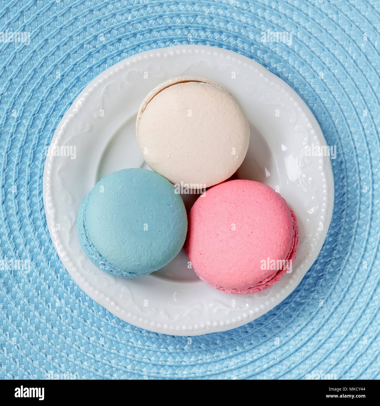 Trois macarons de différentes couleurs et goûts différents dans une assiette blanche, vue du dessus. Fond carré Banque D'Images