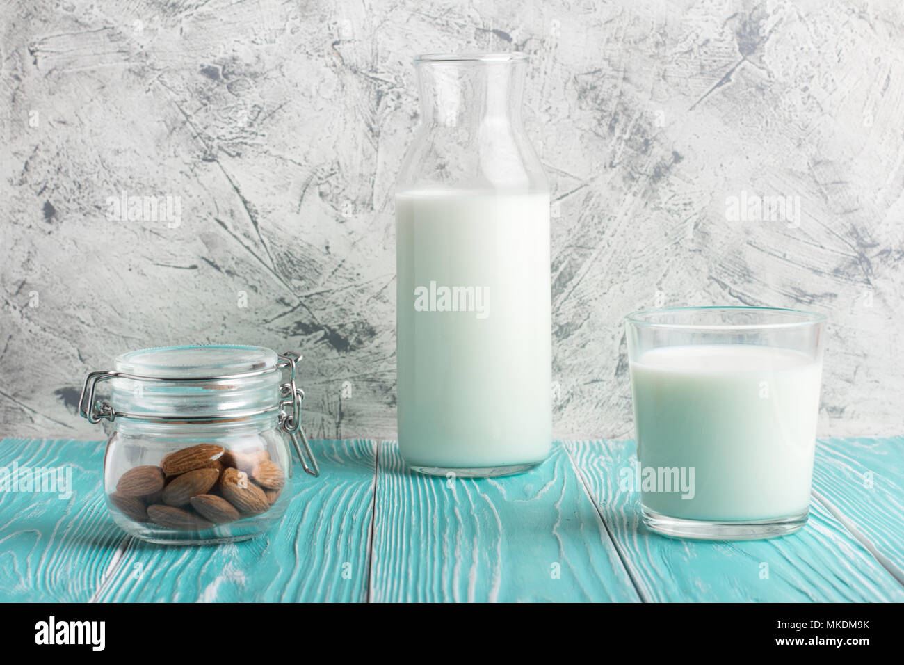 Bouteille de verre avec le lait d'amande et les amandes dans un pot bleu rustique sur table en bois. Vue centrale Banque D'Images