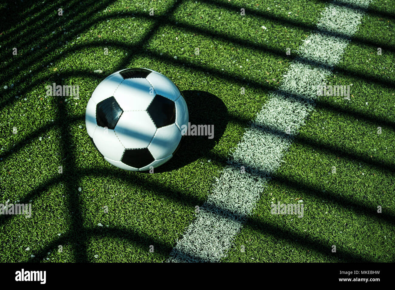 Ballon de football classique noir et blanc avec des ombres sur le terrain d'un but de football artificiel Banque D'Images
