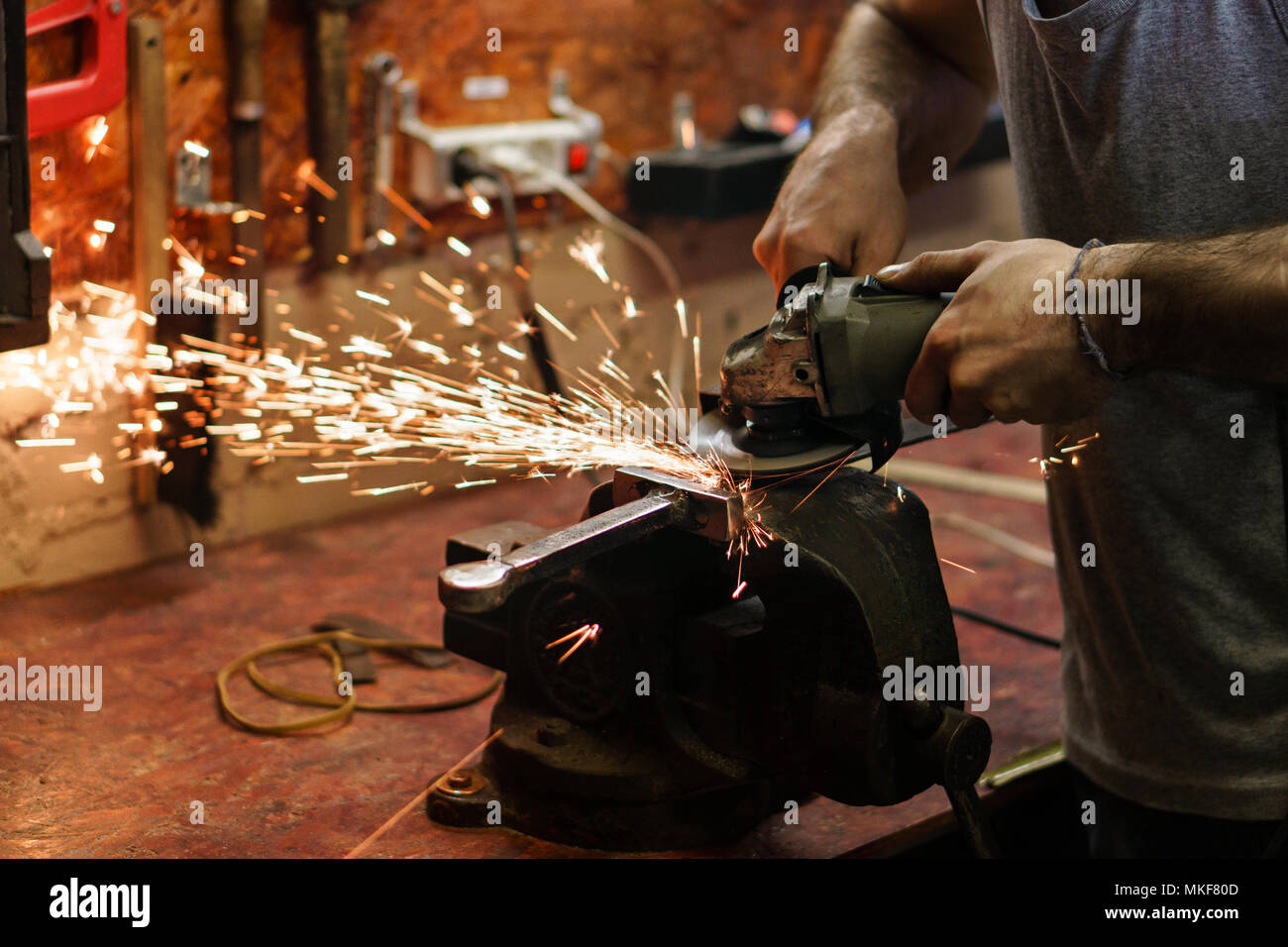 Encaustiques crossguard forgeron de sabre. L'homme travaille en atelier. Il est titulaire d'un broyeur dans ses mains. Banque D'Images