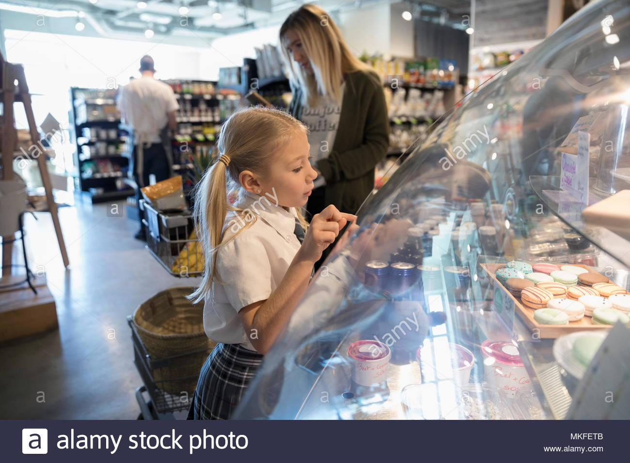 Curieux girl browsing desserts en marché en boulangerie vitrine Banque D'Images