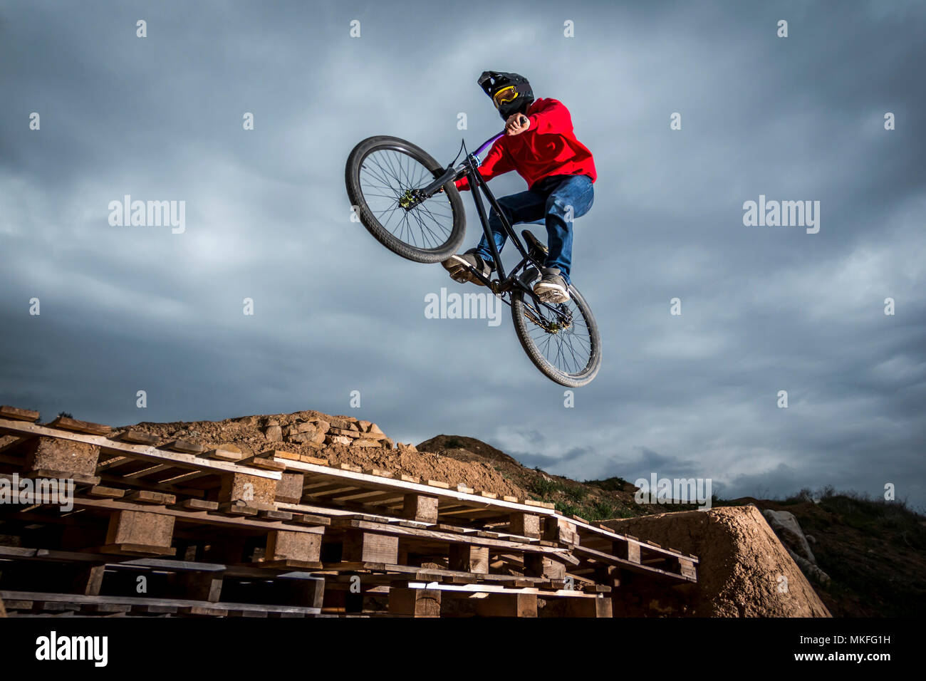 Vue latérale du sportsman sautant par dessus le trou avec palettes et l'exécution de truc sur le vélo Banque D'Images
