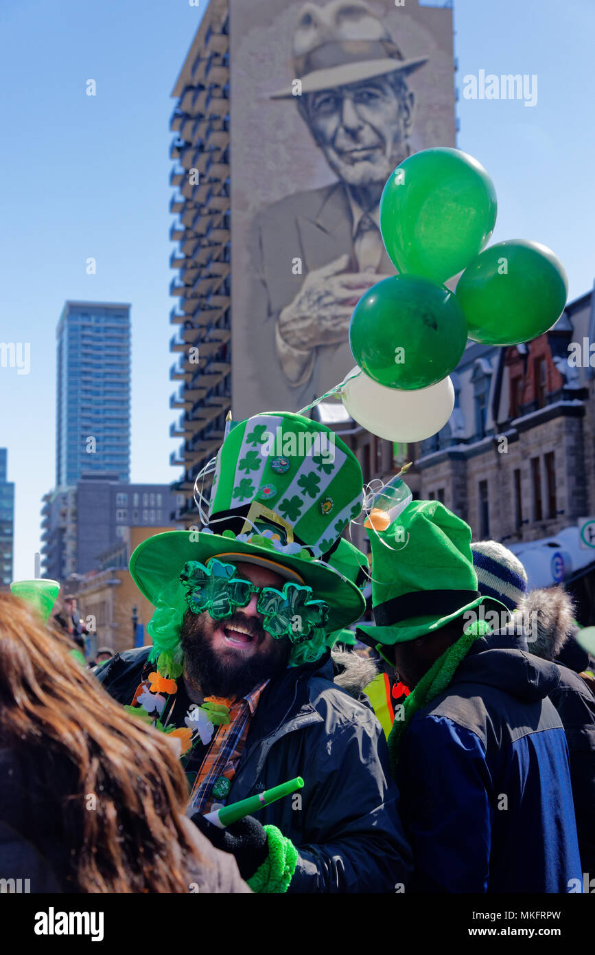 Rire un homme portant des lunettes de soleil en forme de trèfle à la Montreal St Patricks Day Parade, avec le grand portrait de Leonard Cohen derrière Banque D'Images