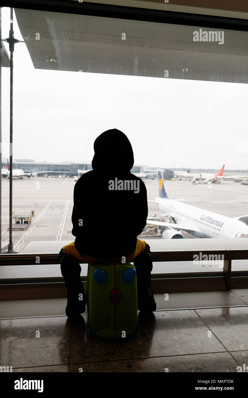 Un jeune garçon (5 ans) était assis sur sa valise à la recherche à l'avions à l'aéroport d'Heathrow Banque D'Images