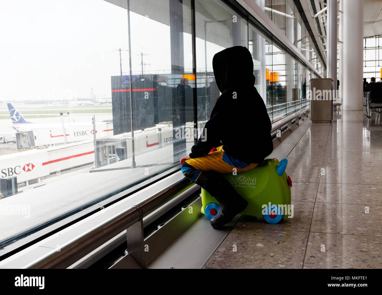 Un jeune garçon (5 ans) était assis sur sa valise à la recherche à l'avions à l'aéroport d'Heathrow Banque D'Images