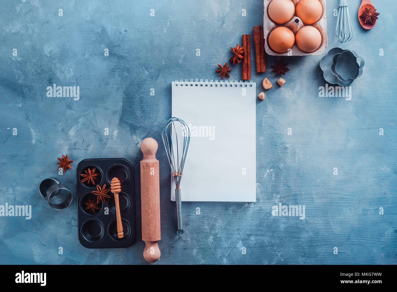 Recette de pâtisserie concept avec outils de cuisson, les ingrédients et un bloc-notes avec des pages blanches sur un fond moderne avec copie espace. Scoops, fouets, emporte-pièce, muffin tin, les oeufs et la cannelle à partir de ci-dessus. Banque D'Images