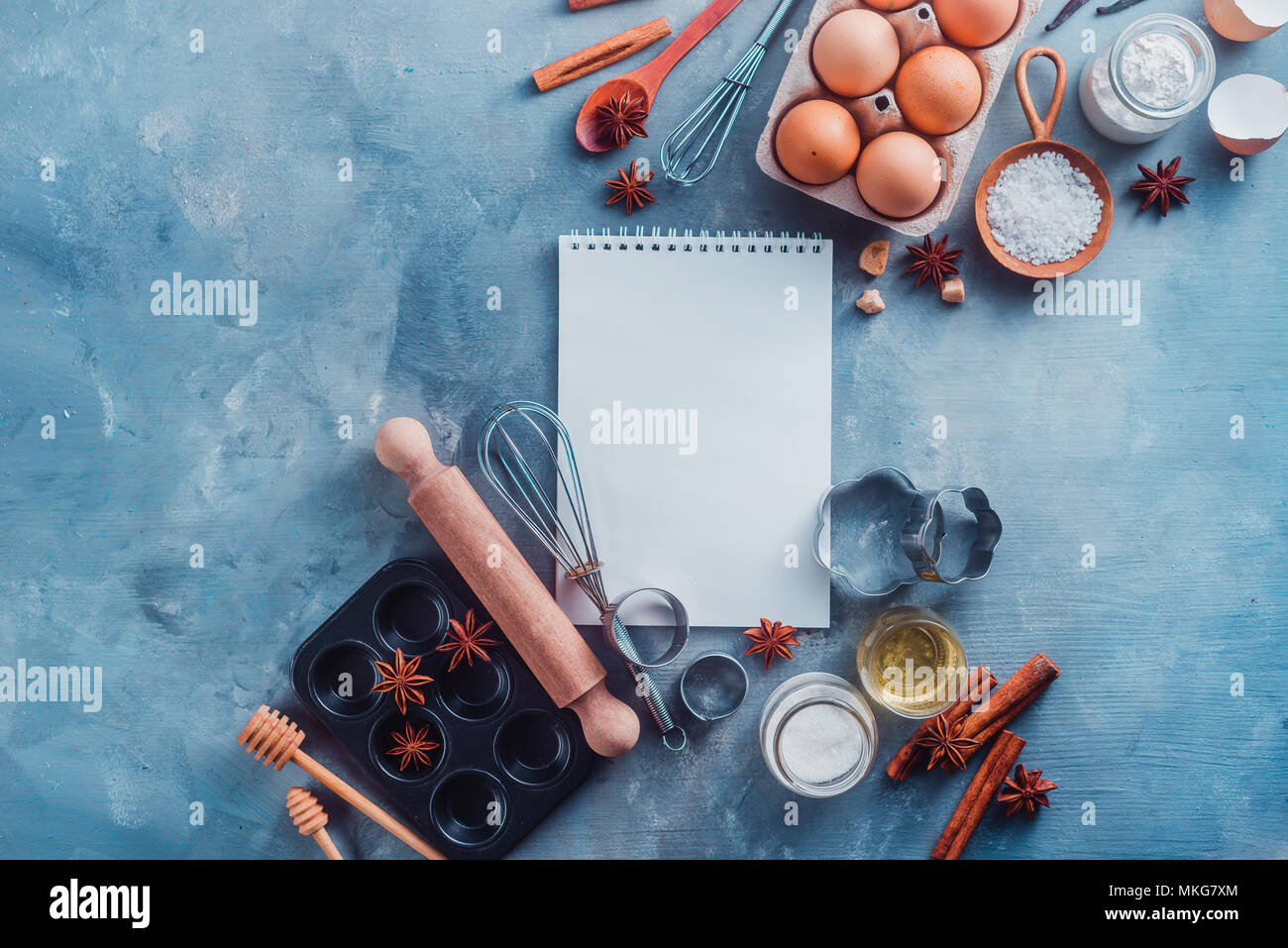 Recette de pâtisserie concept avec outils de cuisson, les ingrédients et un bloc-notes avec des pages blanches avec copie espace. Scoops, fouets, emporte-pièce, muffin tin, oeufs, sucre, farine, l'anis et la cannelle à partir de ci-dessus. Banque D'Images