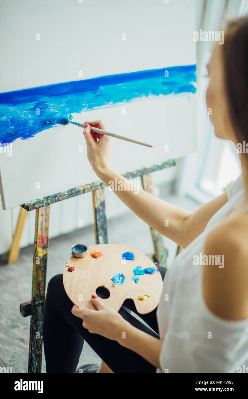 Vue rare de femme peintre avec l'art s'agenouille sur sa palette un dessin , peinture à l'aquarelle bleue. Banque D'Images