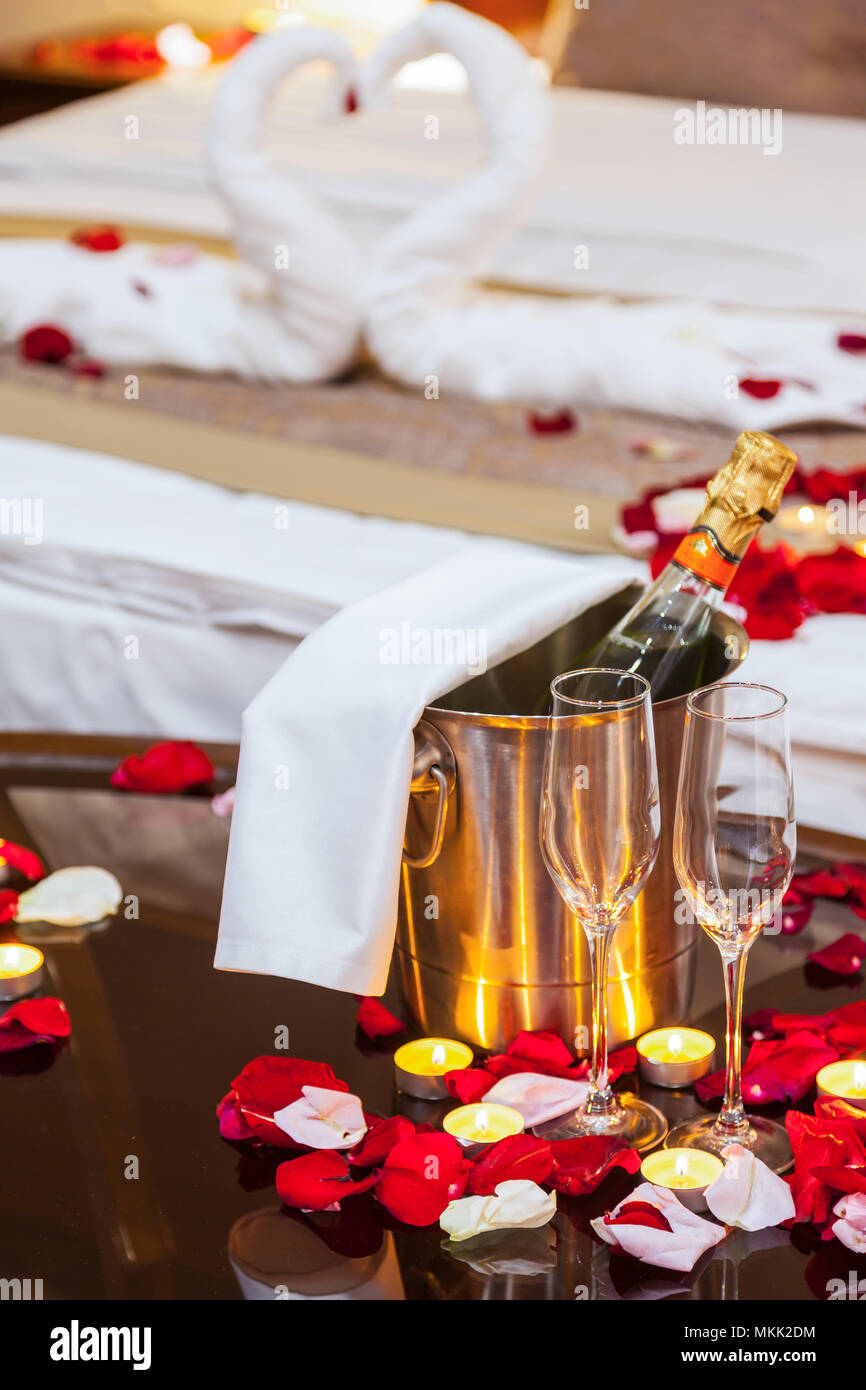 Dîner romantique pour les amoureux : verres de champagne, champagne avec de  la glace dans un seau en métal et des bougies, dans l'arrière-plan un lit  décoré de pétales de rose Photo
