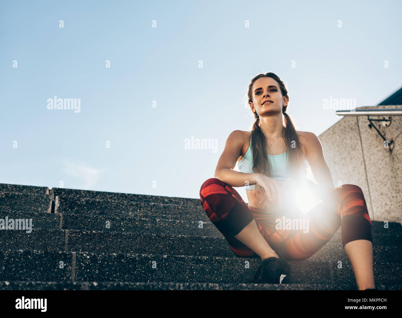 La jeune femme assise sur un escalier extérieur en matinée. En prenant de l'athlète féminine reste après entraînement avec sun flare. Banque D'Images