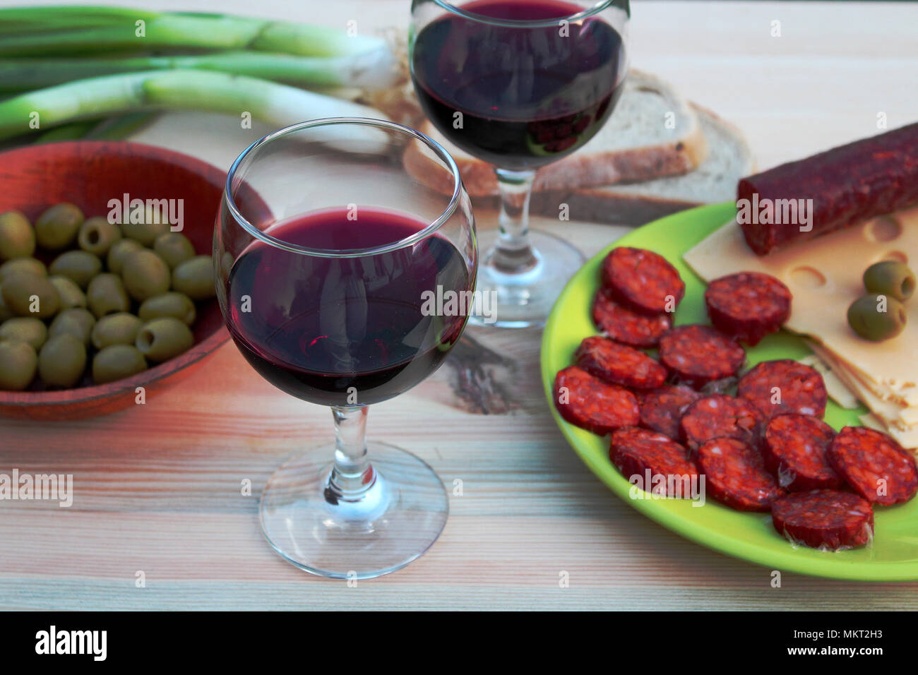 Deux verres de vin rouge avec des saucisses, du fromage et du pain et d'olives vertes sur une table Banque D'Images