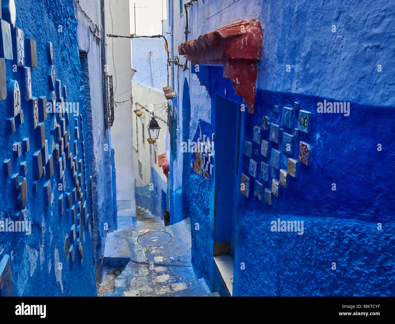 Ouverture étroite entre les murs bleus d'un bâtiment ancien, décoré de carreaux de céramique, Chefchaouen, Maroc. Banque D'Images