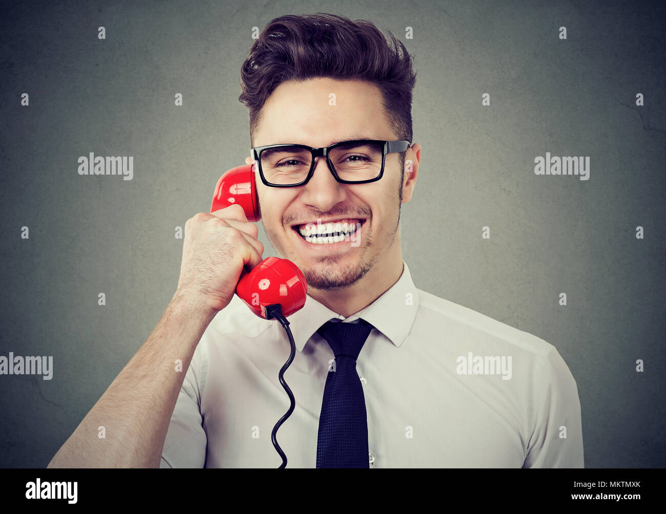 Beau jeune homme à lunettes parler sur un téléphone et appareil photo à rire joyeusement. Banque D'Images