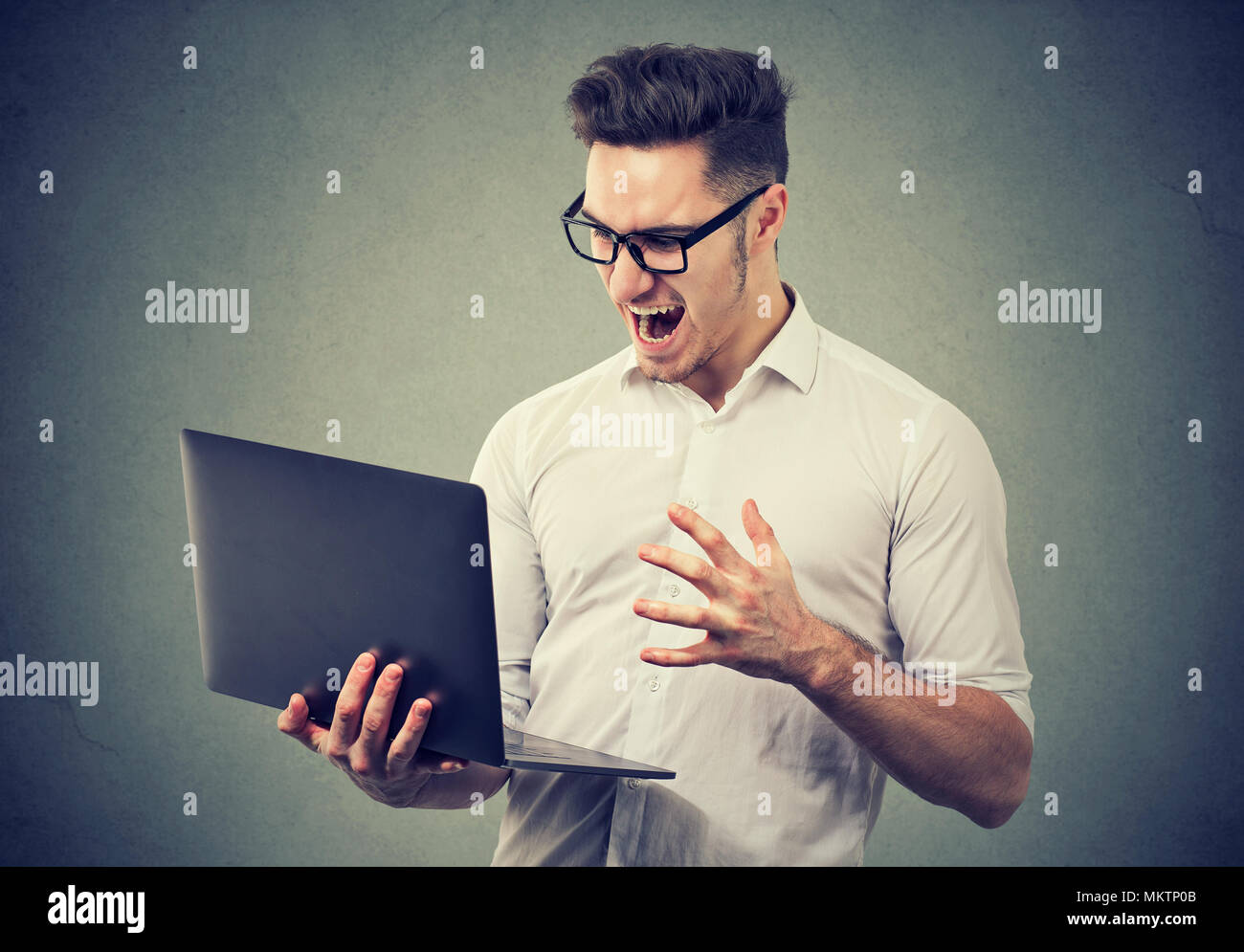 Employé formelle en shirt et lunettes pour ordinateur portable regarder dans beaucoup d'émotion de la colère et de la folie. Banque D'Images