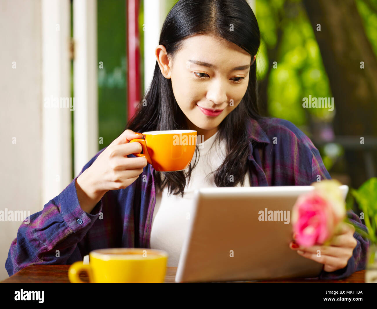 Beautiful young asian woman using digital tablet en buvant un cappuccino au café. Banque D'Images