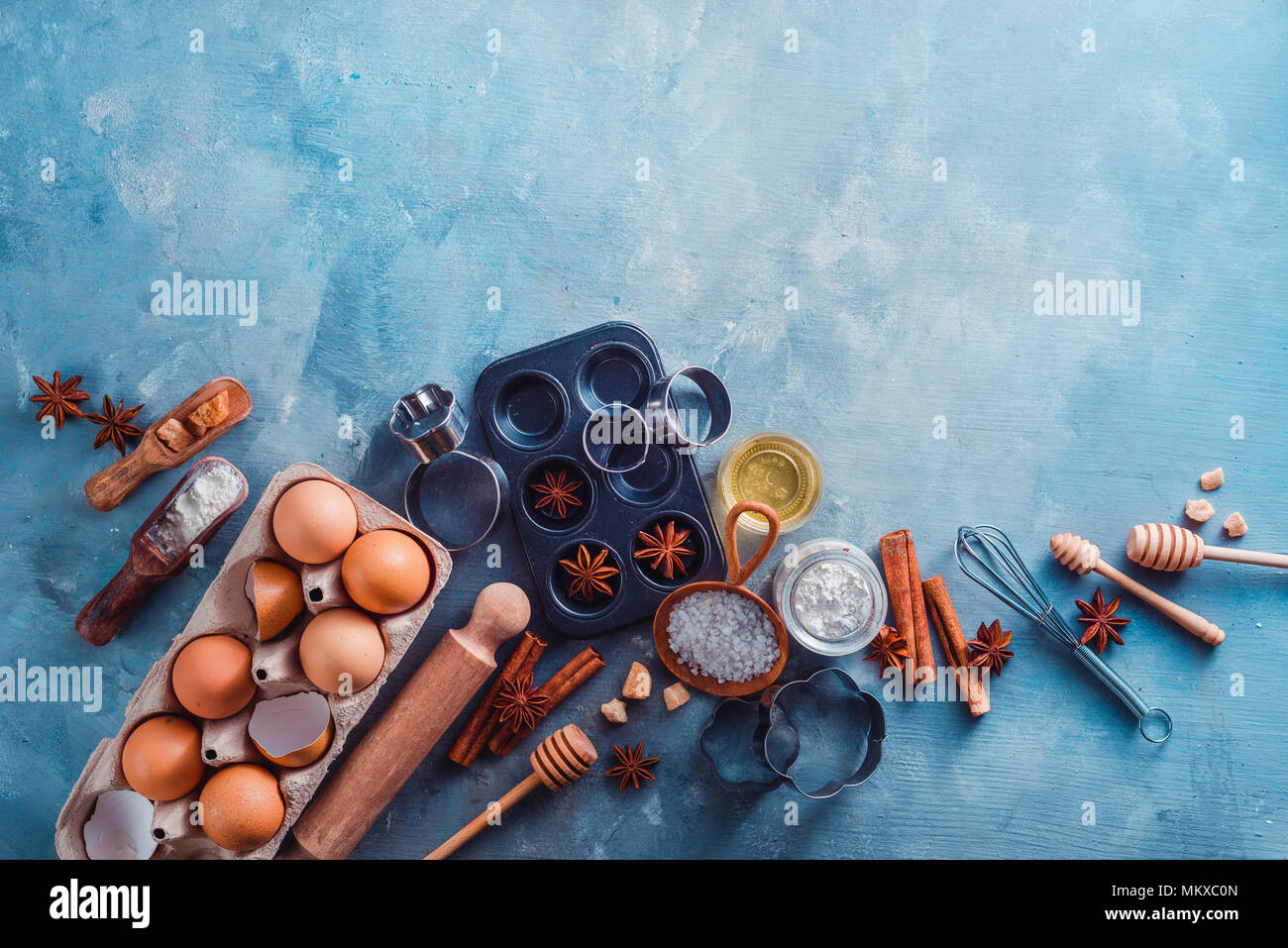 Faire de la pâtisserie avec des mises à plat, pelles, fouets, emporte-pièce, muffin tin, le sucre, la farine, les oeufs et la cannelle sur un fond moderne en béton avec copie espace. Outils de cuisson et des ingrédients à partir de ci-dessus. Banque D'Images