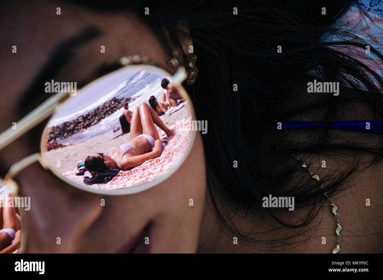 Le verre de lunettes de certains sur une jeune femme reflète une autre femme sur le sable avec l'arrière-plan de la mer Banque D'Images