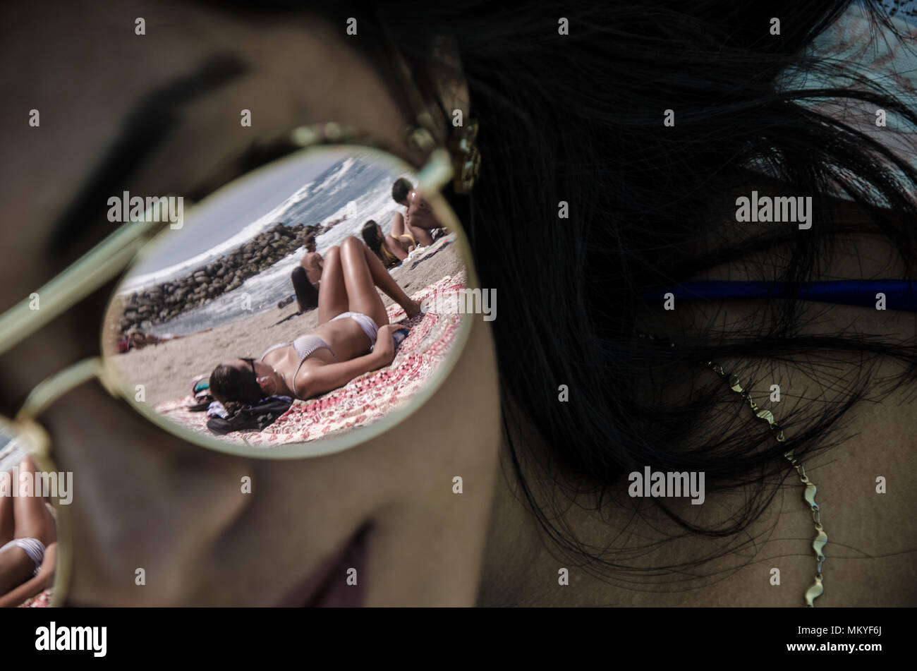 Le verre de lunettes de certains sur une jeune femme reflète une autre femme sur le sable avec l'arrière-plan de la mer Banque D'Images