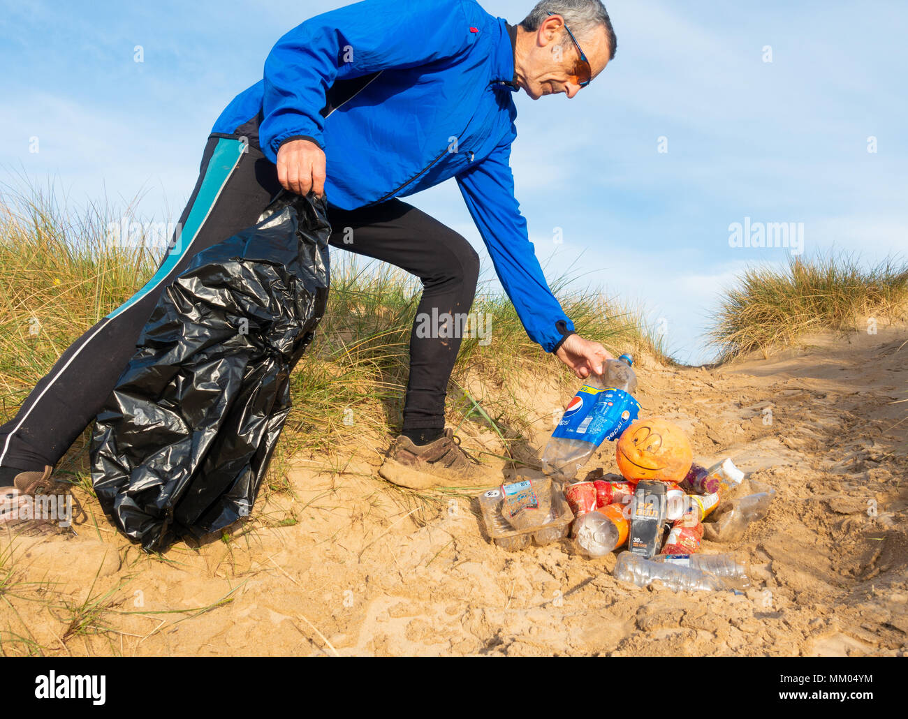 Un Plogging jogger (ramasser les déchets tout en jogging) sur son matin courir à travers les dunes de sable.UK Banque D'Images