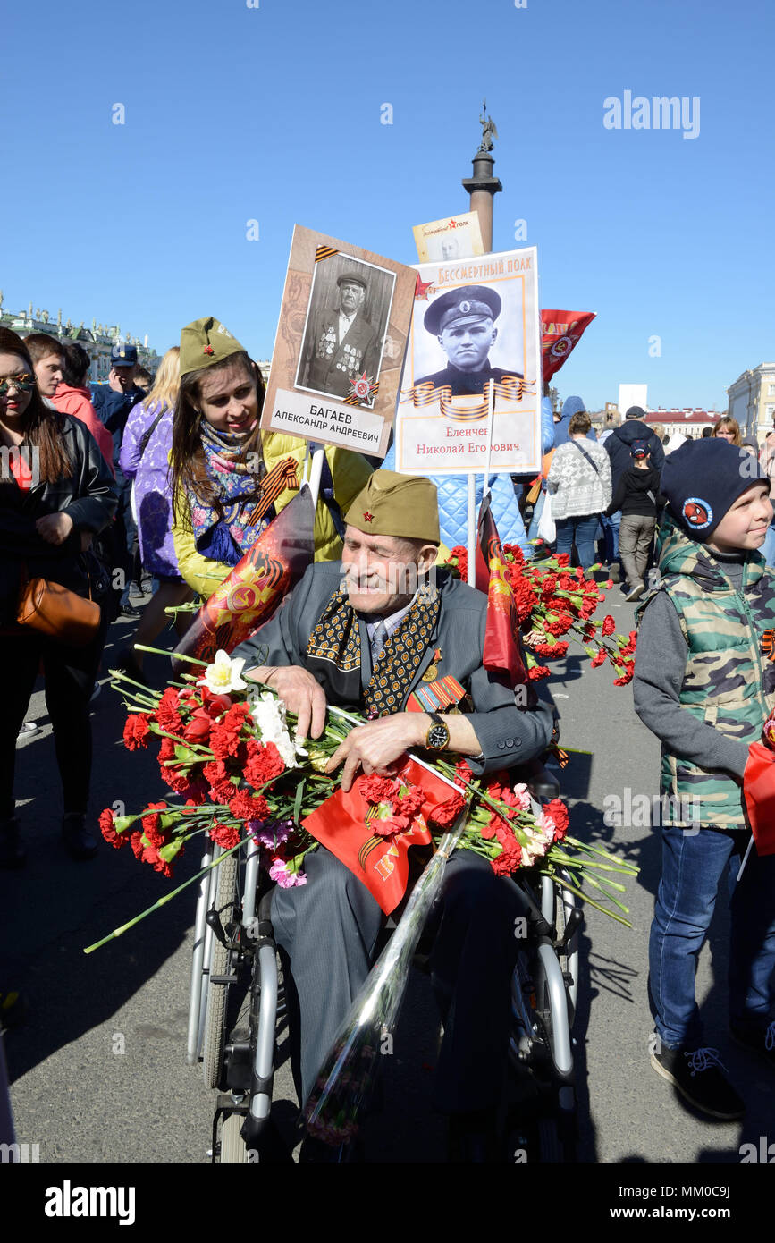 Un vieux vétéran, participant à la Seconde Guerre mondiale, avec des médailles, des ordres, des promenades sur la victoire de la journée, la Russie avec des fleurs dans les mains sur un fauteuil roulant Banque D'Images