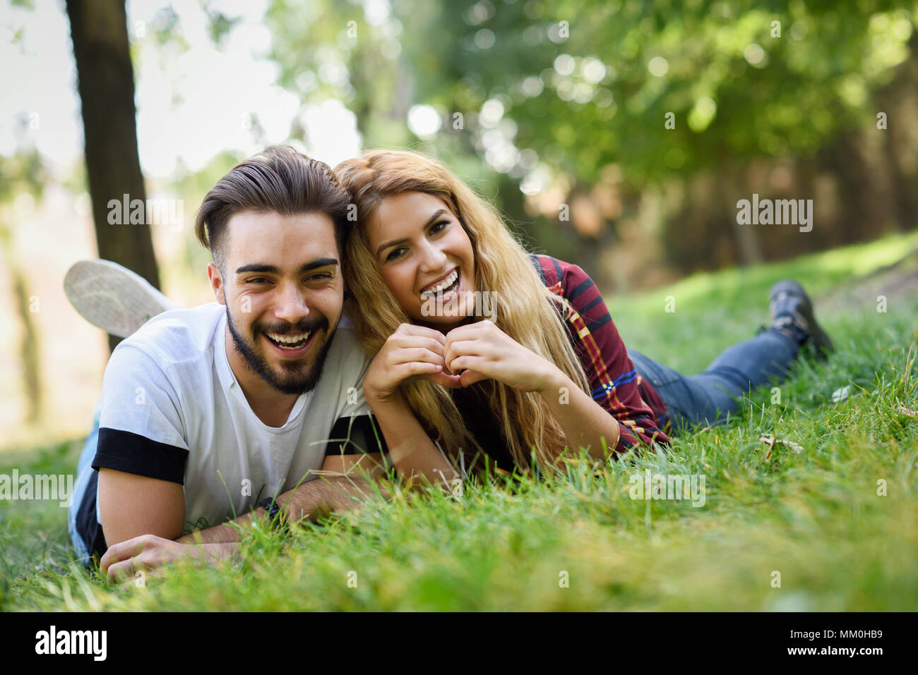 Beau jeune couple portant sur l'herbe dans un parc urbain. Homme de race blanche et femme portant des vêtements décontractés. Femme blonde. Banque D'Images