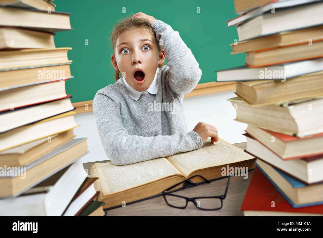 Écolière est choqué. Photo de petite fille avec une bouche ouverte et de grands yeux autour des livres. Le concept de l'éducation Banque D'Images