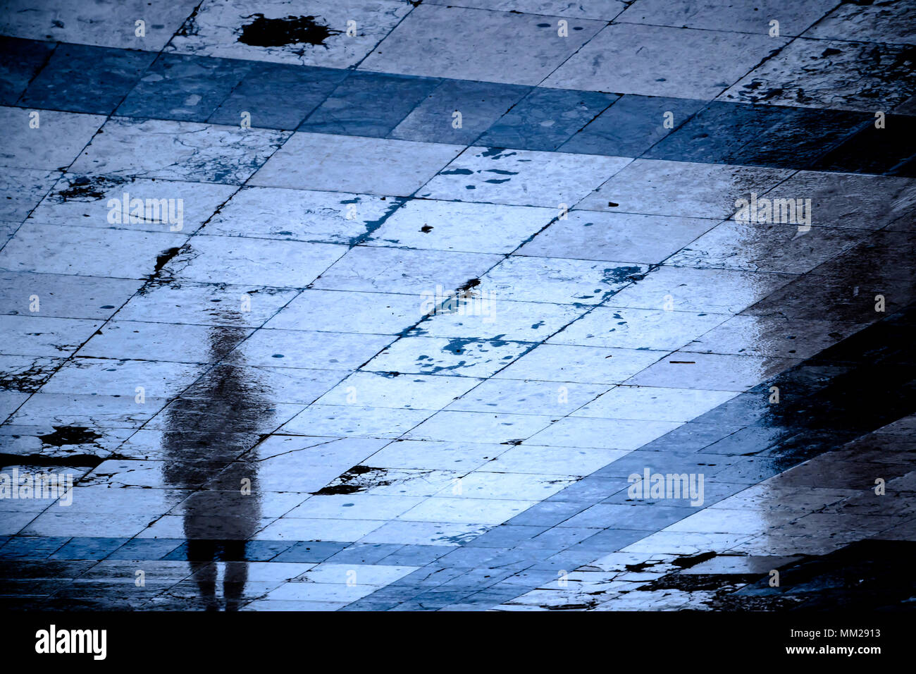 Réflexion floue ombre d'une personne qui marche la ville rue trottoir à motifs sur une nuit pluvieuse Banque D'Images