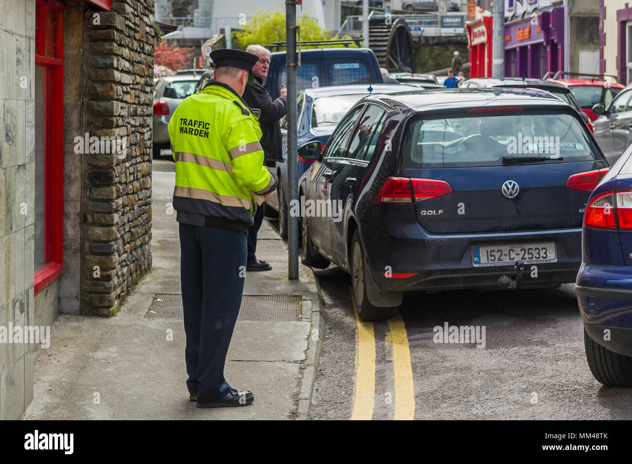 Trafic irlandais Préfet émet un ticket de parking pour une voiture qui est garé sur double lignes jaunes et le trottoir à Bantry, dans le comté de Cork, Irlande. Banque D'Images