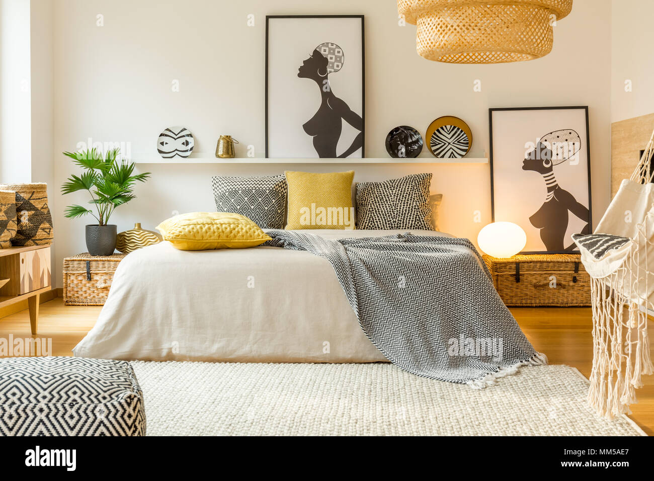 À motifs jaunes et des oreillers au lit dans une chambre moderne d'intérieur chaleureux avec des affiches et des plantes Banque D'Images