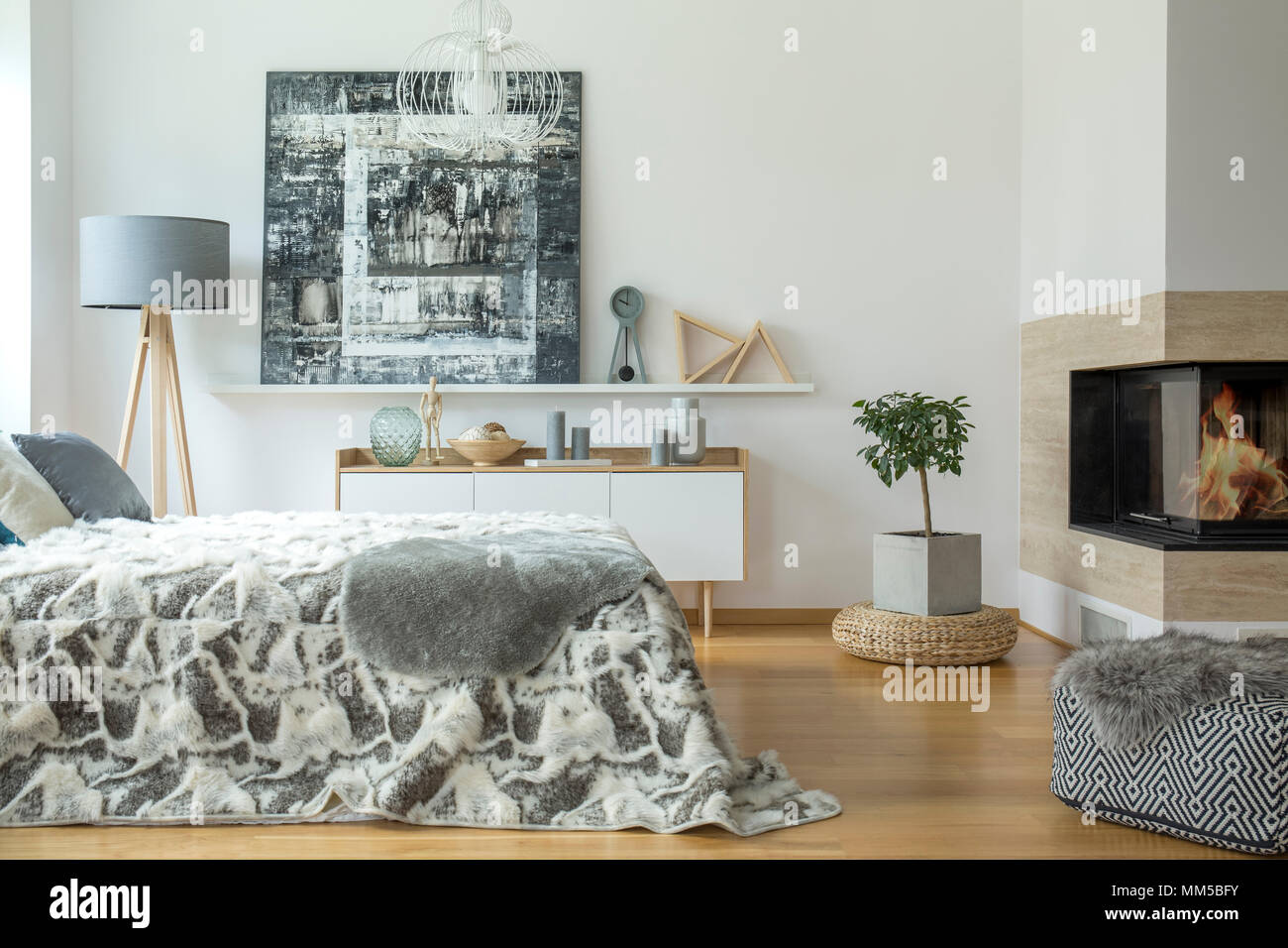 Fourrure gris sur lit et pouf dans une chambre chaleureuse avec la peinture d'intérieur, plante et cheminée Banque D'Images