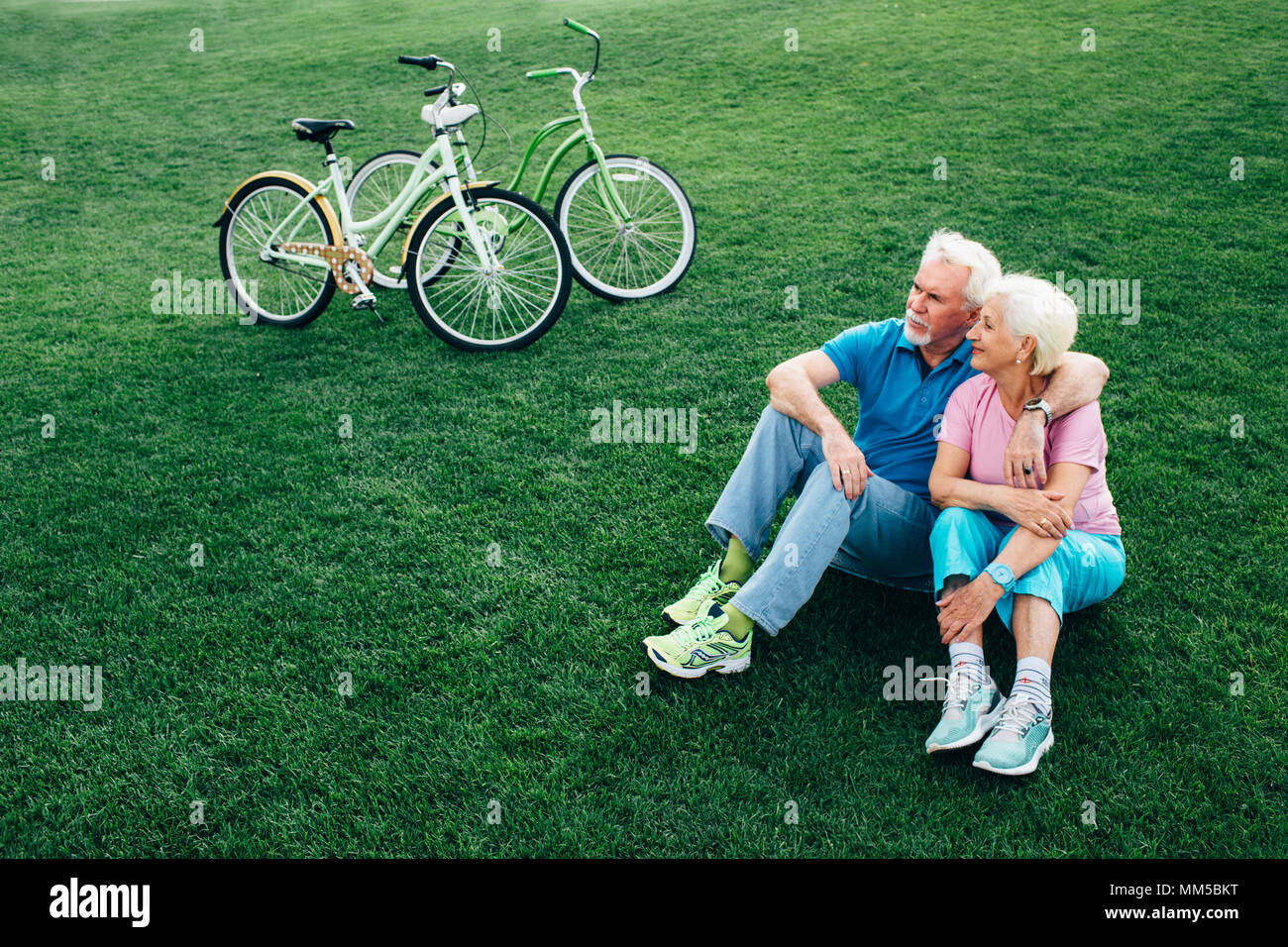 Beau vieux couple est assis sur l'herbe, après la bicyclette Banque D'Images