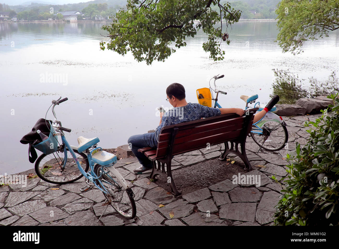Surf homme / contrôle son téléphone portable tandis que sa petite amie prend un power nap, Lac de l'Ouest, à Hangzhou, Province de Zhejiang, Chine Banque D'Images