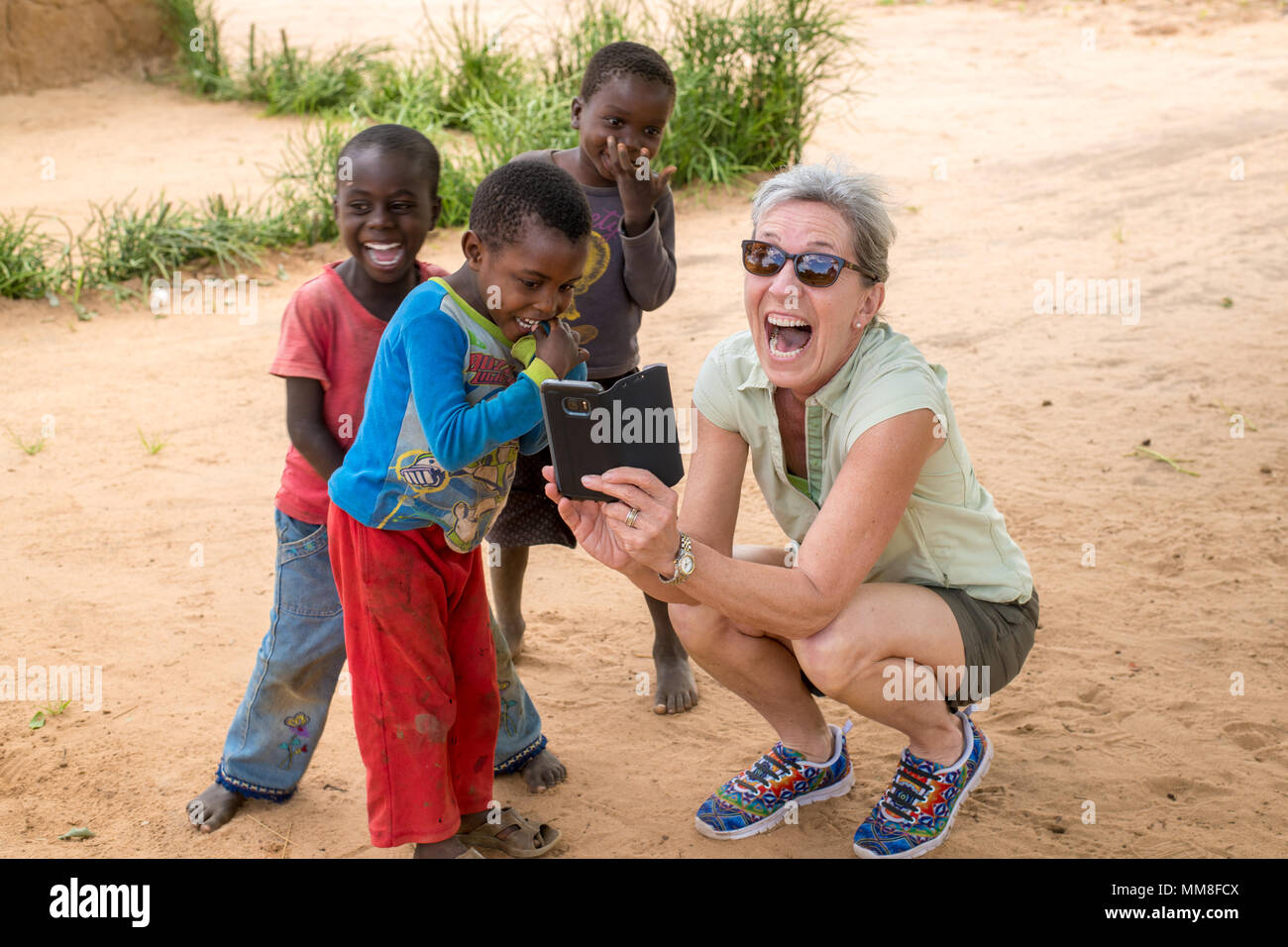 Une femme avec excitation partage quelque chose sur son téléphone avec un groupe de jeunes garçons. Livingstone, Zambie Banque D'Images