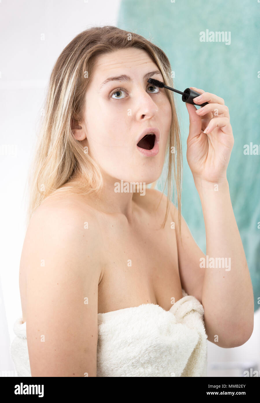 Portrait de jeune femme ouvre la bouche tandis que le mascara et le maquillage fait dans la salle de bains Banque D'Images