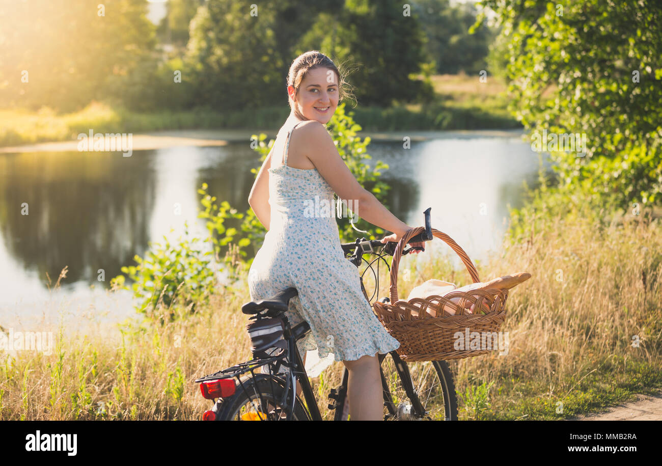 Beautiful smiling young woman posing on vintage bicycle dans champ à susnet Banque D'Images