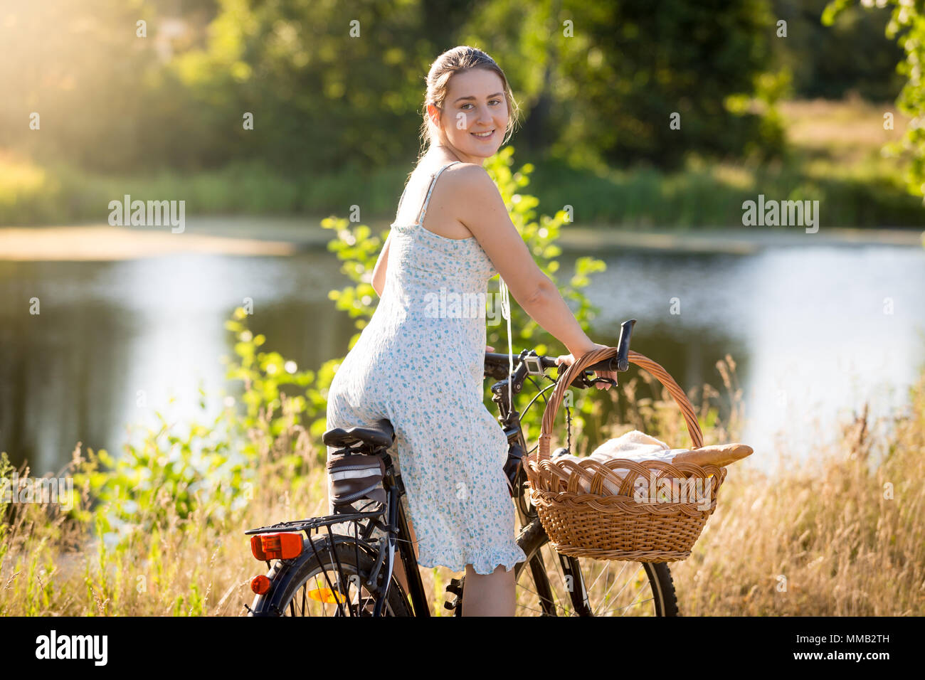 Portrait of smiling young woman riding bicycle in field et à la caméra sur l'épaule dans Banque D'Images