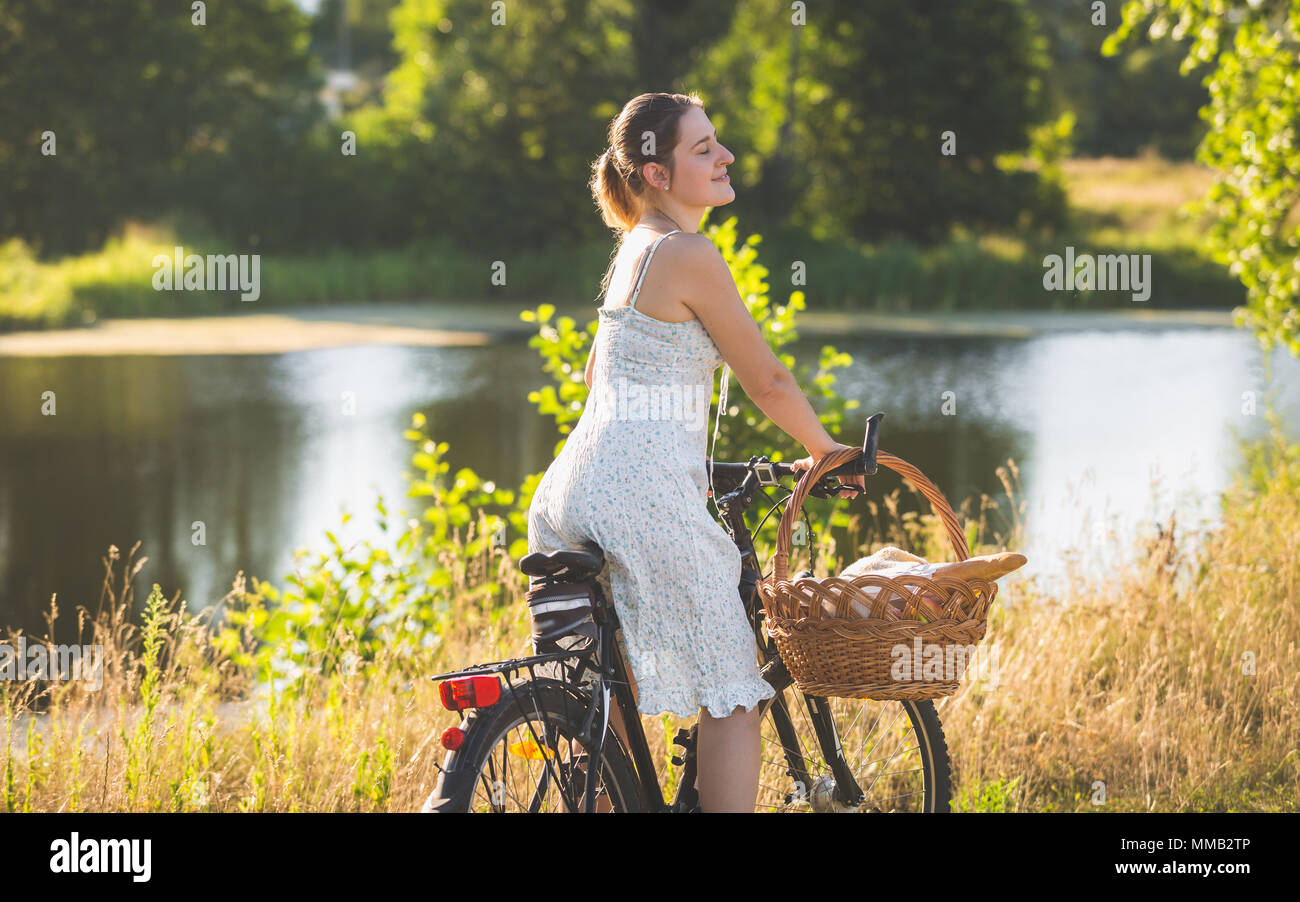 Portrait aux couleurs de belle jeune femme en robe d'été courte riding bicycle at river Banque D'Images