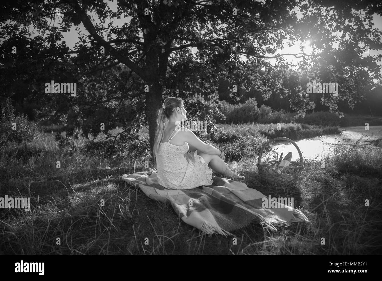 Image en noir et blanc de la jeune femme se détendre sous arbre à river et à la recherche au soleil du soir Banque D'Images