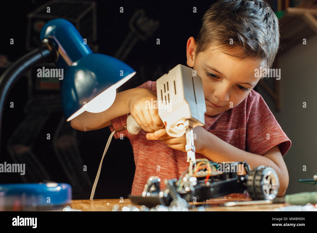 Portrait d'un garçon intelligent d'apprendre à souder à la maison. Enfant à l'aide d'un pistolet à souder et travailler sur sa voiture robotique. Banque D'Images