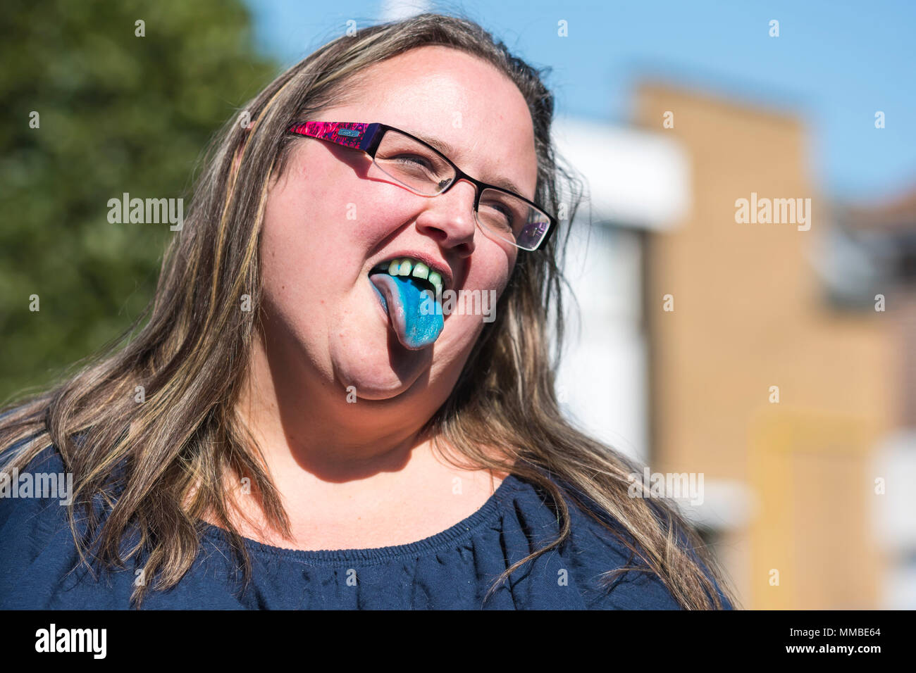 Woman sticking tongue out après avoir bu un verre bleu slush puppy, montrant de bleuissement sur sa langue et des dents, tout en souriant en été. Heureux concept. Banque D'Images