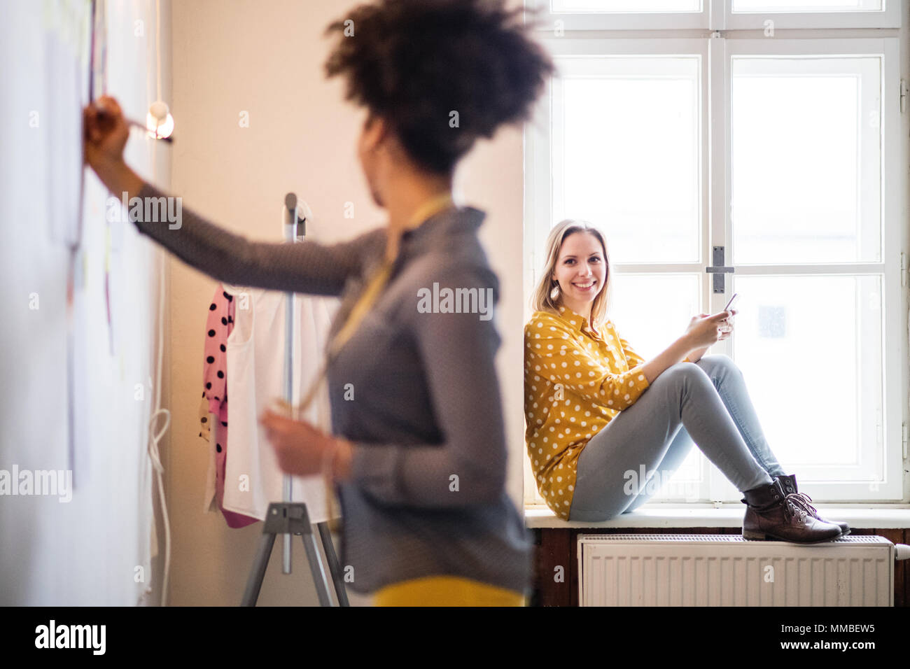 Les jeunes femmes créatives avec le smartphone en studio, entreprise de démarrage. Banque D'Images