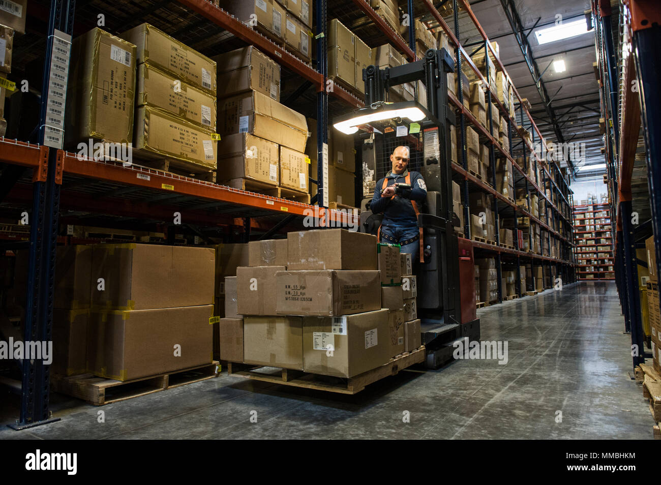Employé de l'entrepôt de porter un harnais de sécurité tandis que opeating motorisé un stock picker dans une allée entre les grands casiers de boîtes de carton holding produit o Banque D'Images
