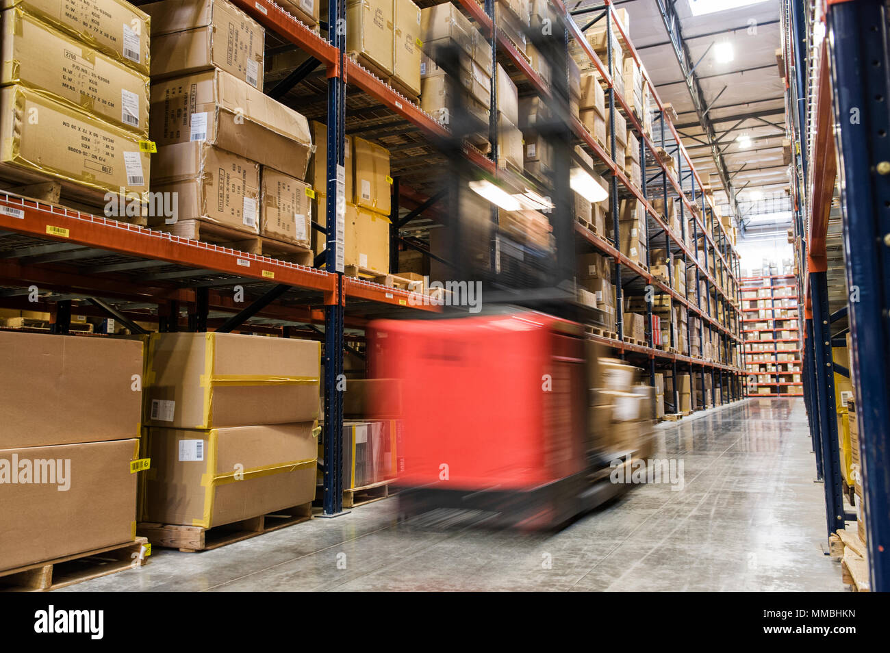 Trouble d'un stock picker motorisé entre les allées de cartons sur palettes gerbées sur de grands casiers dans un grand entrepôt de distribution. Banque D'Images