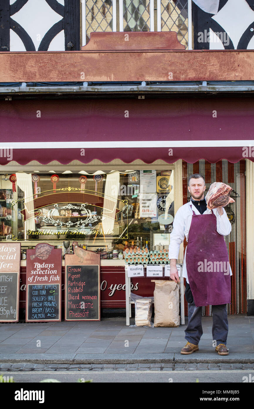 Homme portant un tablier, debout sur le trottoir devant une boucherie, transportant un grand morceau de boeuf sur son épaule. Banque D'Images