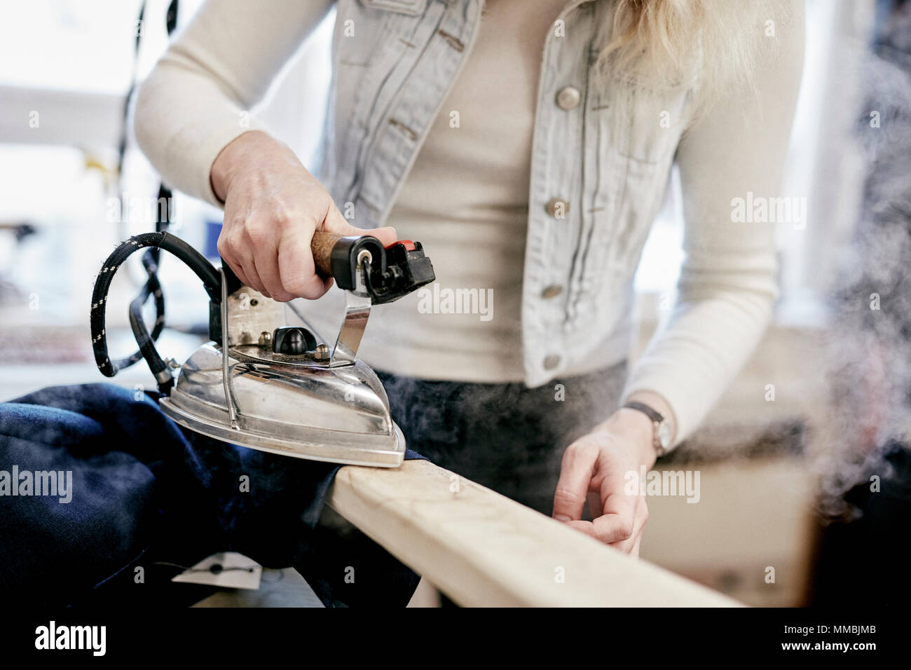 Une femme à l'aide d'un fer à repasser à vapeur sur une nouvelle veste, appuyant sur le fait nouveau vêtement. Banque D'Images