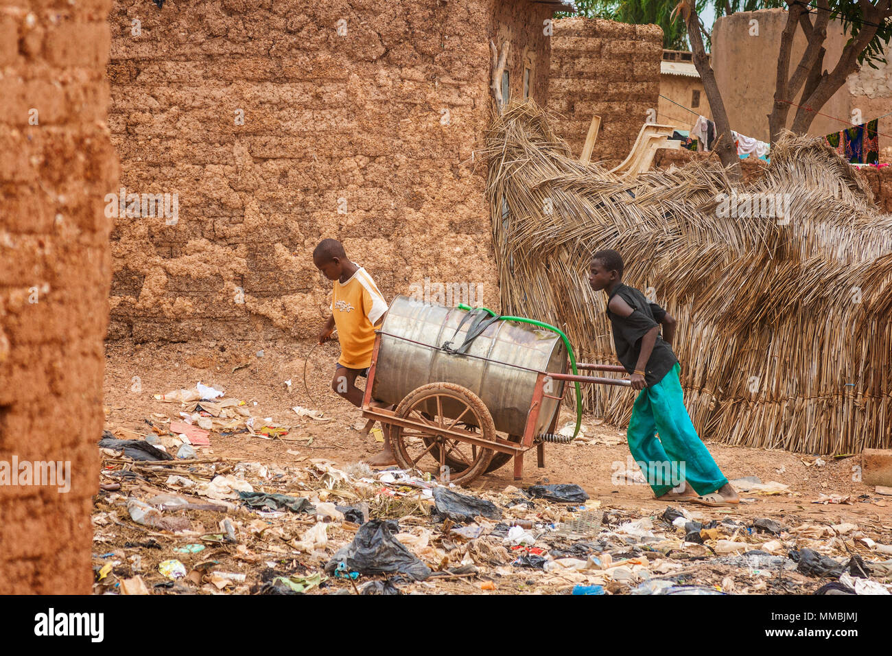 Deux jeunes garçons du remorquage d'un peut d'eau sur roues dans les bidonvilles de Ouagadougou afin de distribuer l'eau aux habitants, le Burkina Faso. Banque D'Images