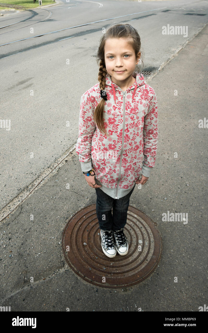 Enfant Girl standing dans le centre de la trappe métallique vide sur la rue en milieu urbain Banque D'Images