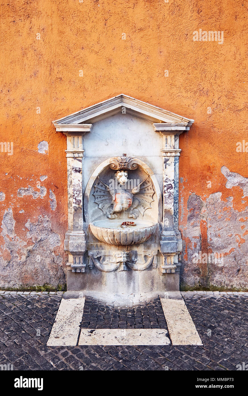 Petite fontaine d'eau potable avec la sculpture et la décoration en pierre en mauvais état mur peint, Rome. Banque D'Images