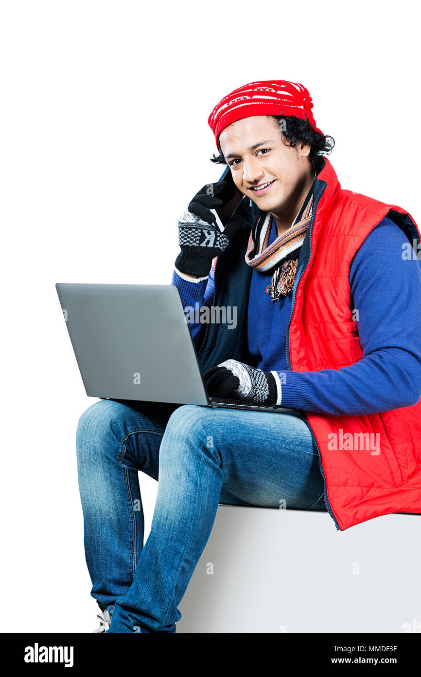 Un jeune homme les vêtements d'hiver à l'aide d'ordinateur portable et parle Mobile-Phone Banque D'Images