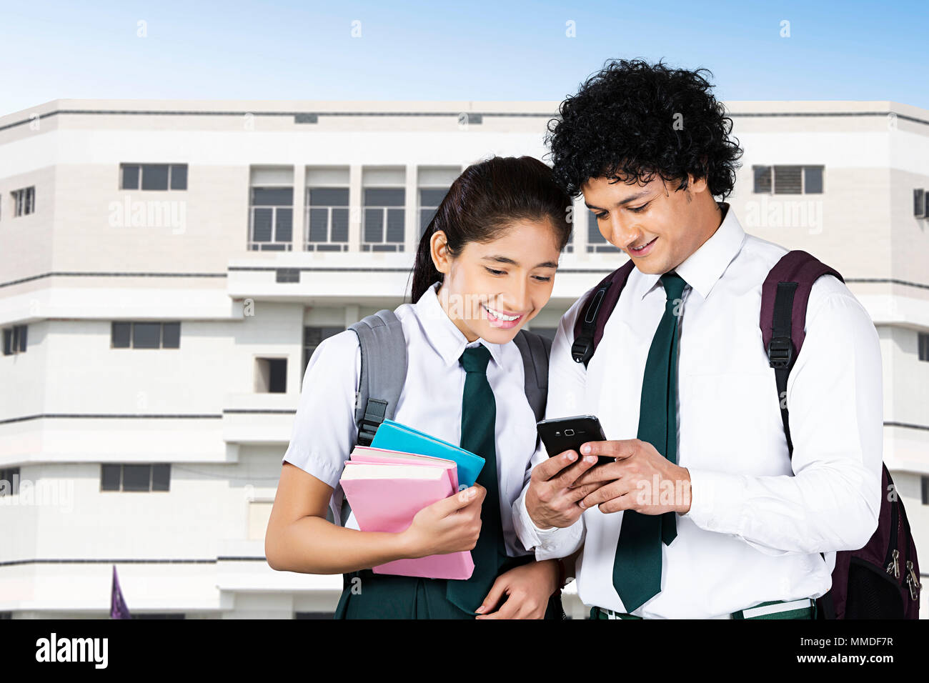 Deux étudiants du secondaire Text-Messaging Mobile-Phone Lecture à l'extérieur du bâtiment de l'école Banque D'Images